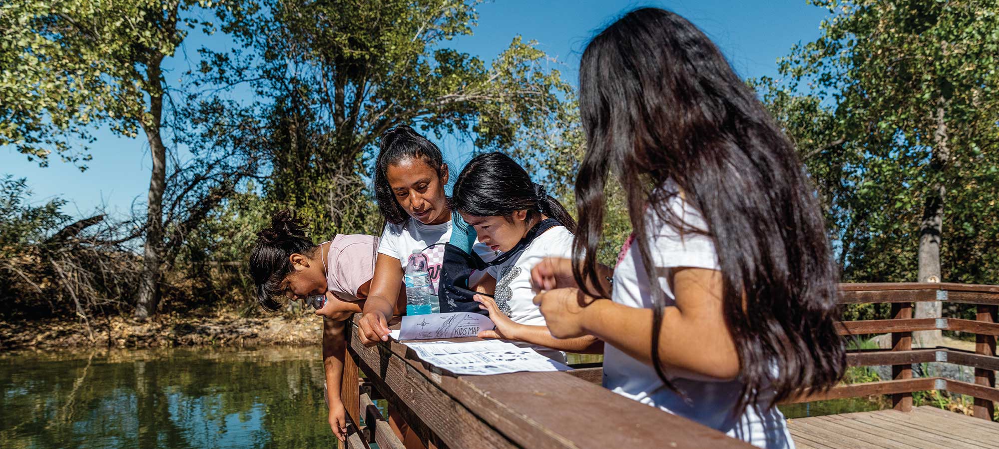 A woman and small girls look at a map while overlooking a scenic lake